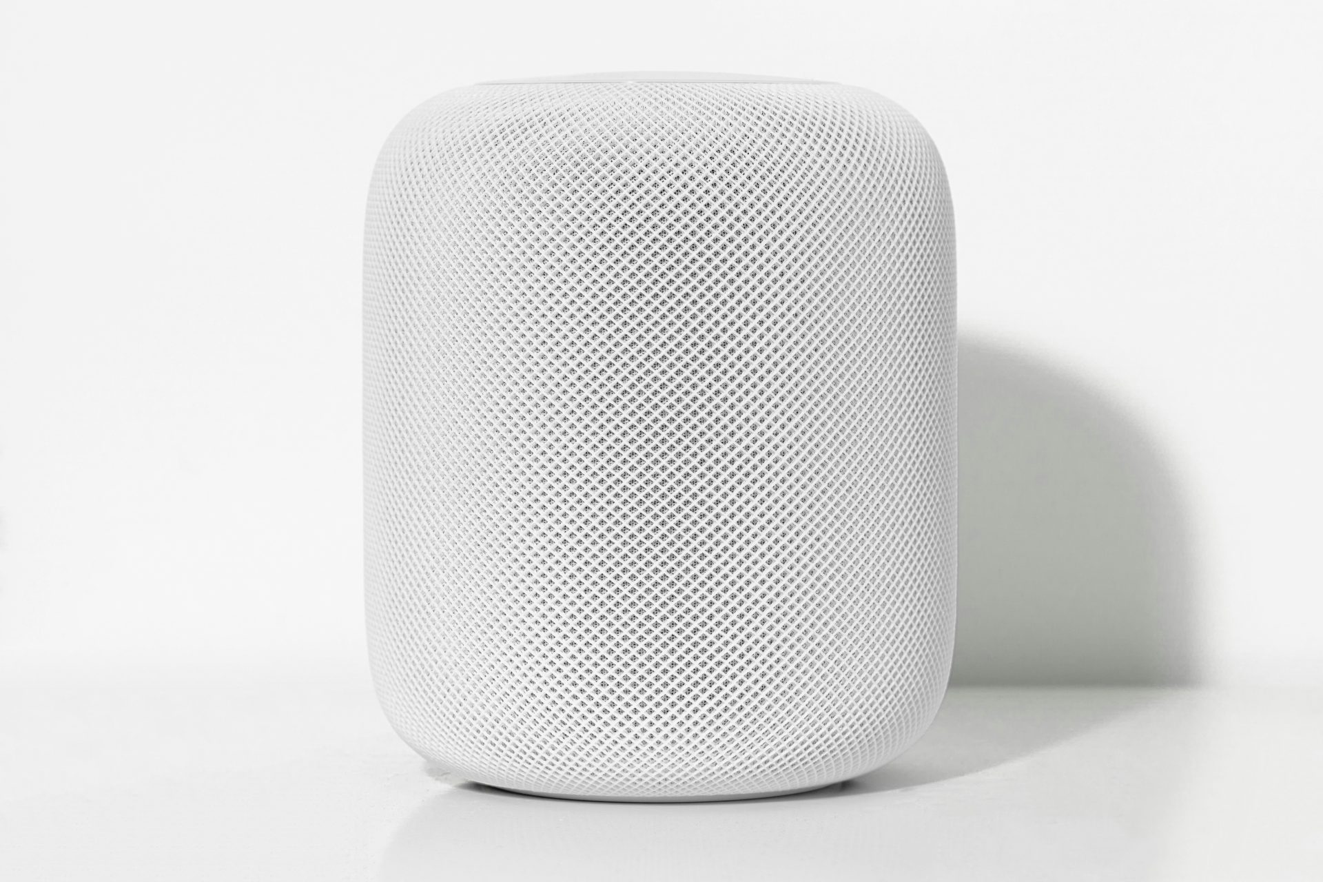 A white cylindrical Apple HomePod smart speaker is centered against a white background.
