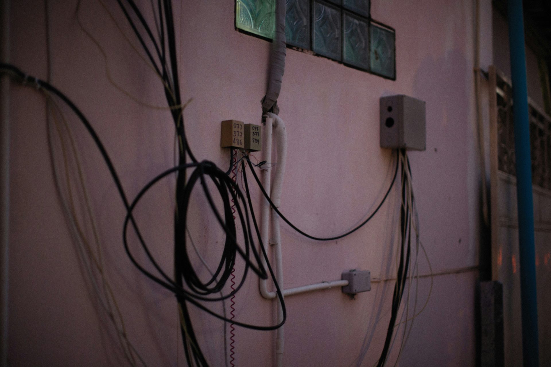 A chaotic tangle of black and white cables covers a light-colored wall, connected to various utility boxes and a speaker.