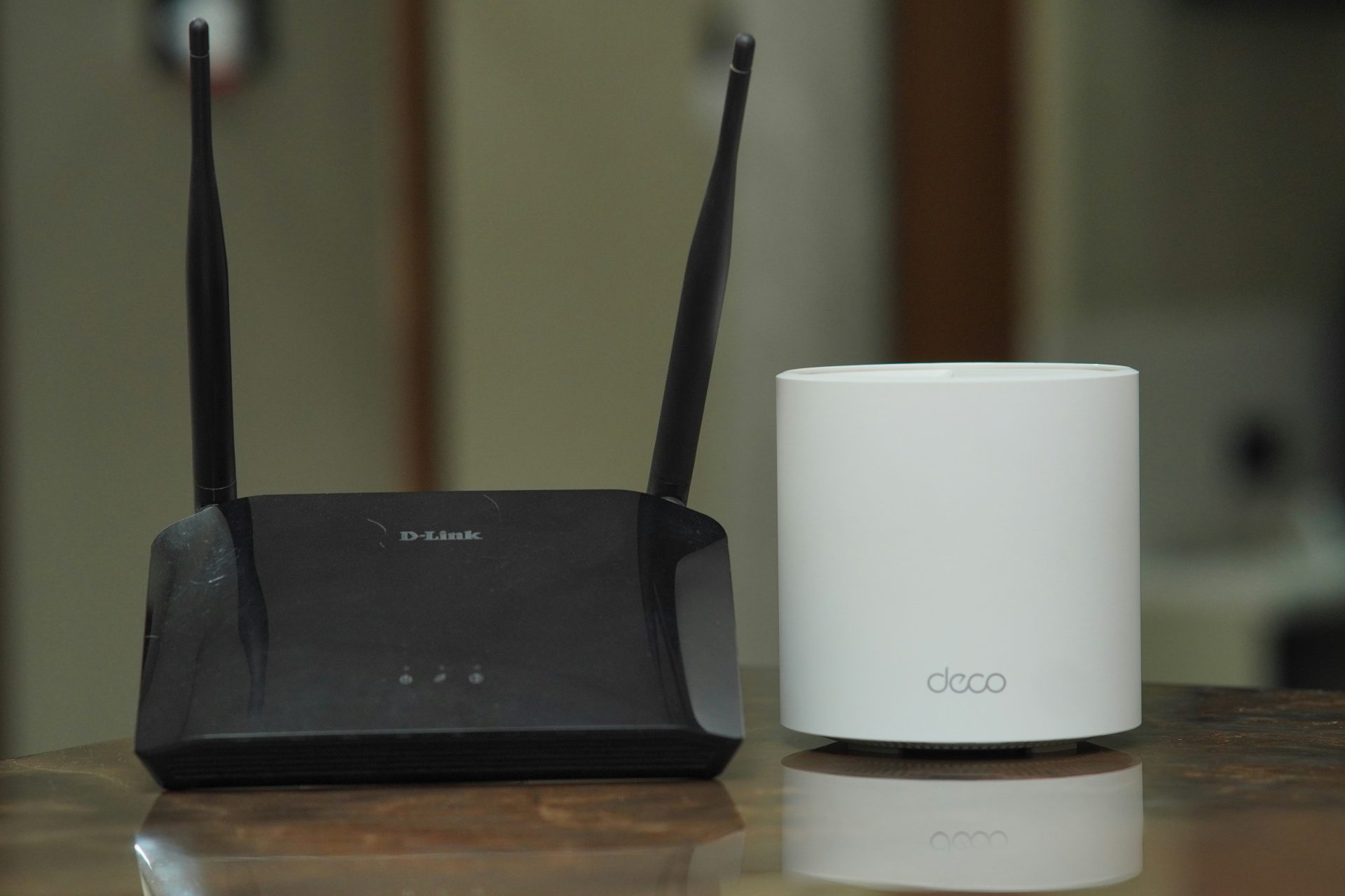 A black D-Link router with two antennas sits next to a white cylindrical Deco mesh Wi-Fi device.