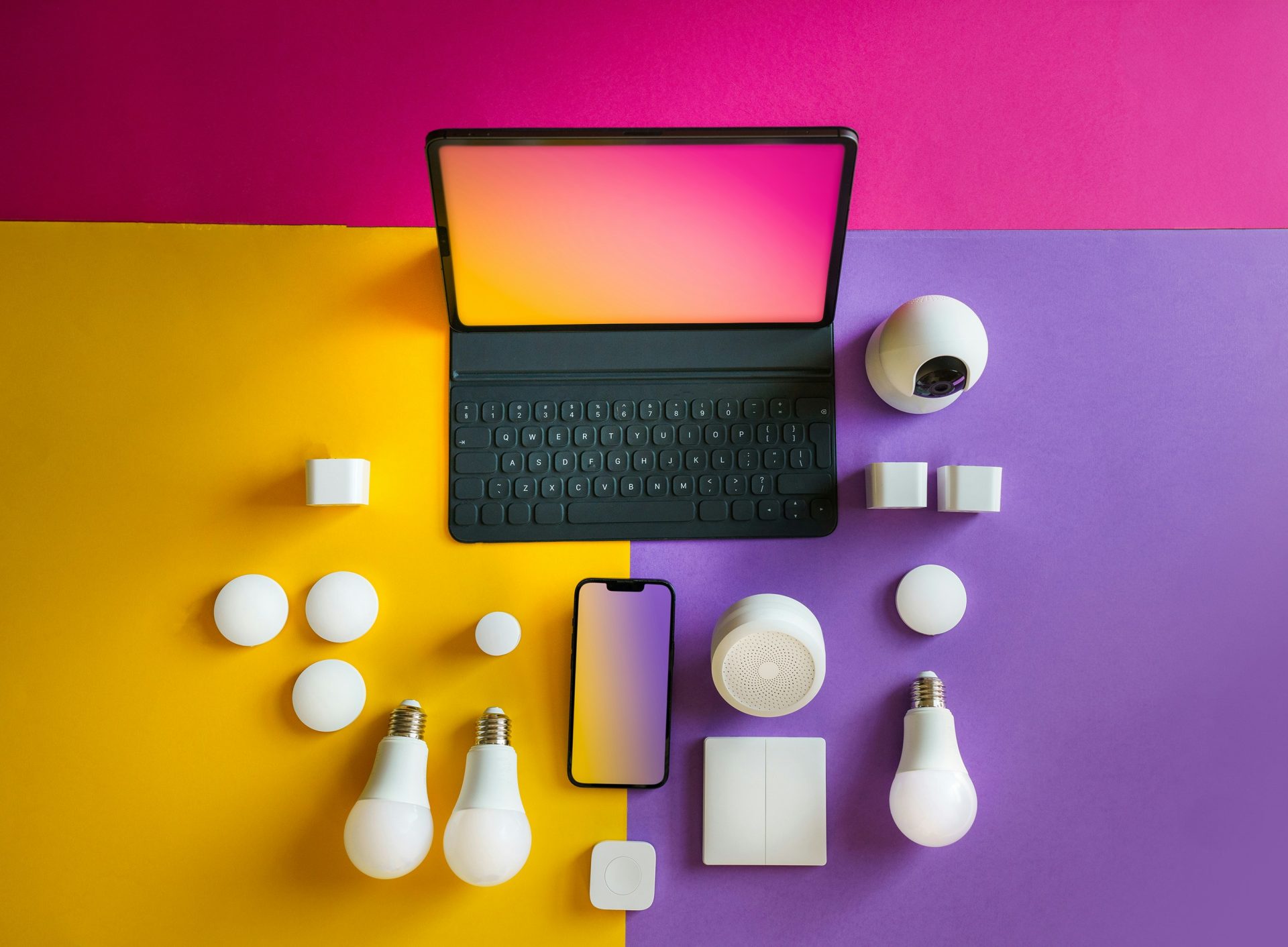 An overhead flat lay displays smart home devices, including a tablet, smartphone, security camera, light bulbs, and various sensors, arranged on a yellow and purple background.